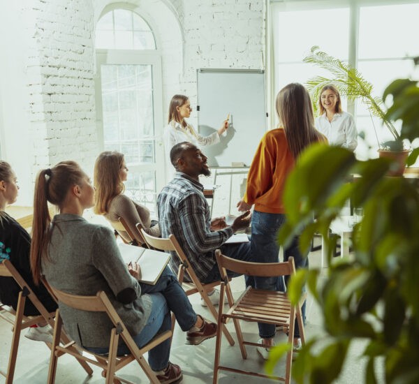 Grupo de personas reunidas escucha a una mujer. 